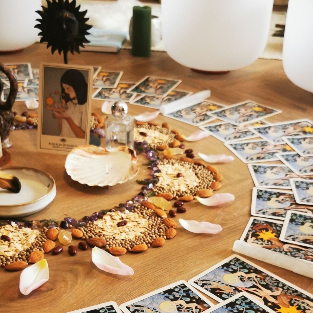 Rituel lunaire avec mandala de graines, pétales et cartes oracles pendant un cercle de femmes à Paris.